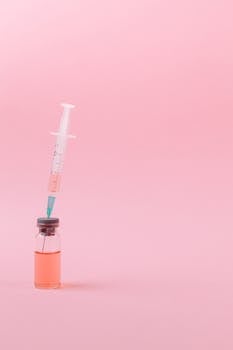 Sterilized syringe drawing vaccine from a vial on a pink backdrop.