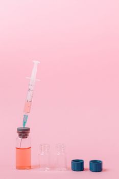 粉红色背景上的小瓶中，注射器正在提取液体，这表示医疗场景