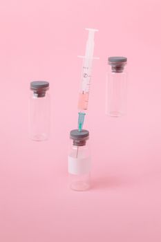 以预防接种为主题，垂直拍摄粉红色背景上的疫苗小瓶和注射器