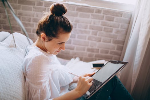 Focused young woman using a tablet with stylus indoors, illustrating remote work lifestyle.