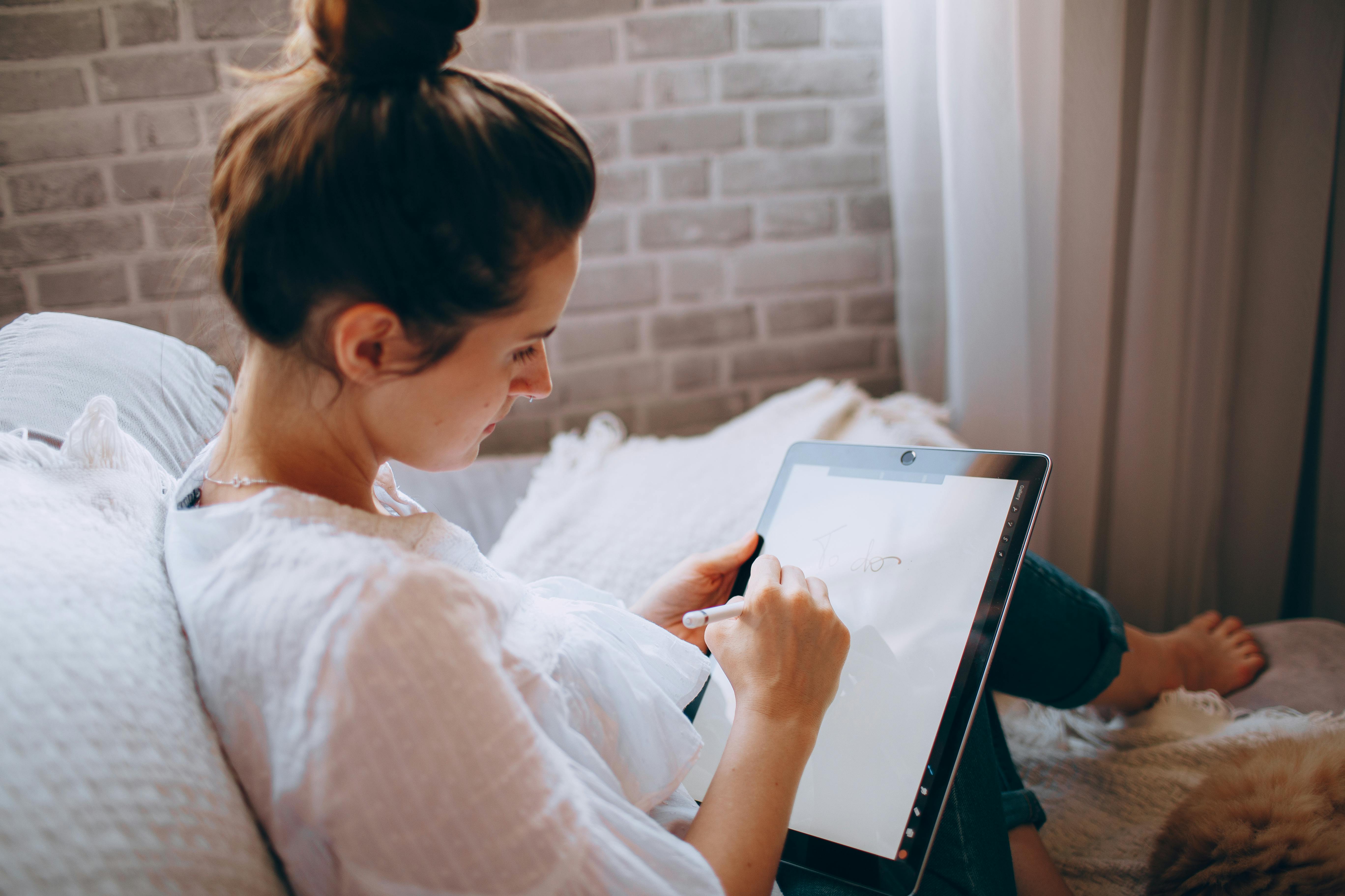 Woman drawing on a tablet while lounging comfortably in a cozy indoor setting.
