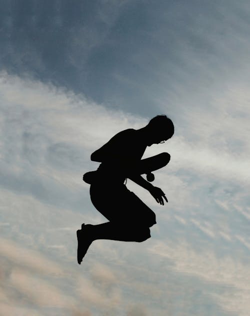 Silhouette of Man Jumping While Holding Skateboard