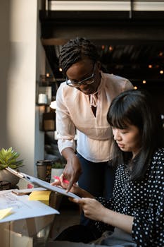 Two women collaborate in a modern office space, focused on creativity and teamwork.