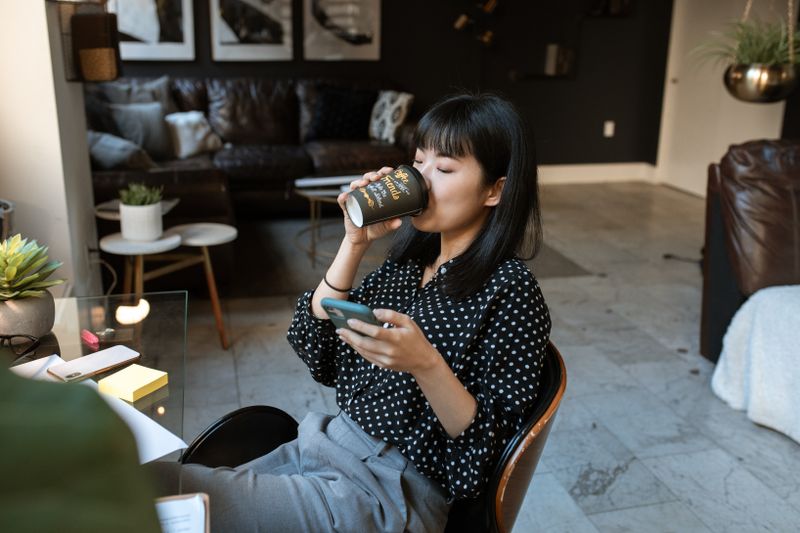 Woman relaxing with a cup of coffee while checking her smartphone in a cozy living room