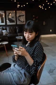 在柔和的灯光下，一位女士在室内微笑着享受智能手机上的休闲时光