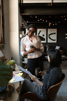 Two professional women discussing a project in a stylish, modern office setting with coffee.