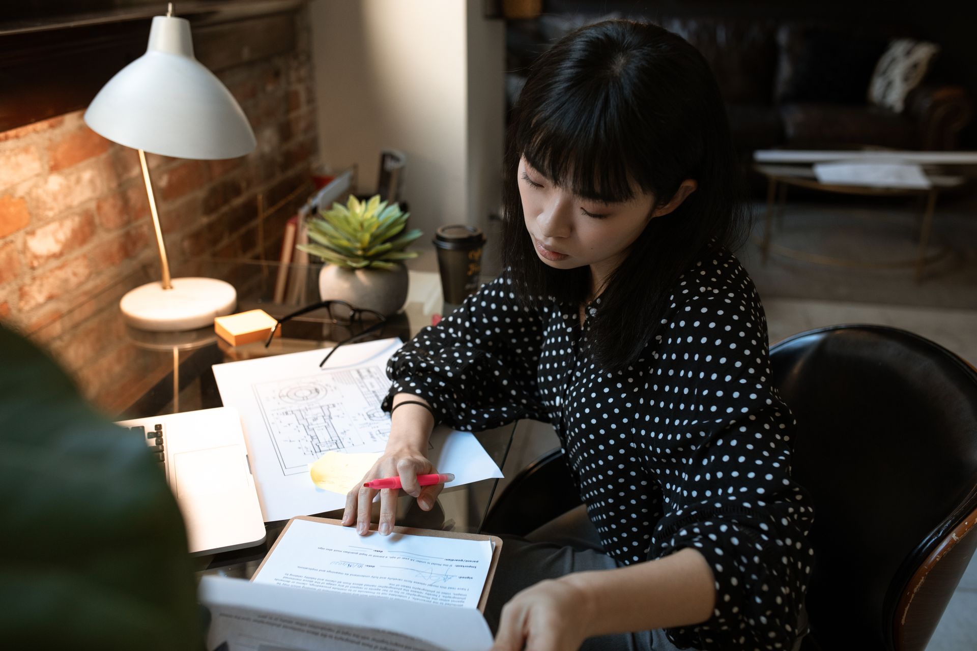 Focused young woman working at a stylish home office desk with papers and a laptop.