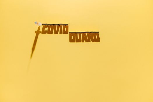 Minimalist visual of a syringe and shadow text 'Covid Guard' on yellow background.