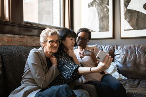 Free Three women of different ethnicities taking a selfie on a sofa in a cozy indoor setting. Stock Photo