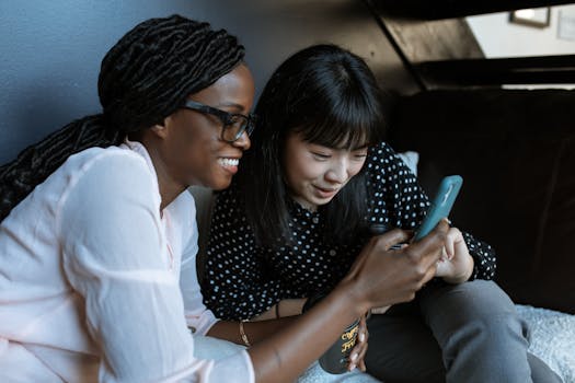 Two women relaxed on a sofa, sharing and enjoying moments on a smartphone.