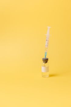 将注射器放在疫苗小瓶上，对着亮黄色背景