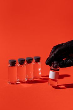 红色背景上，一只戴着手套的手和一堆疫苗小瓶，象征着医疗保健和疫苗接种工作