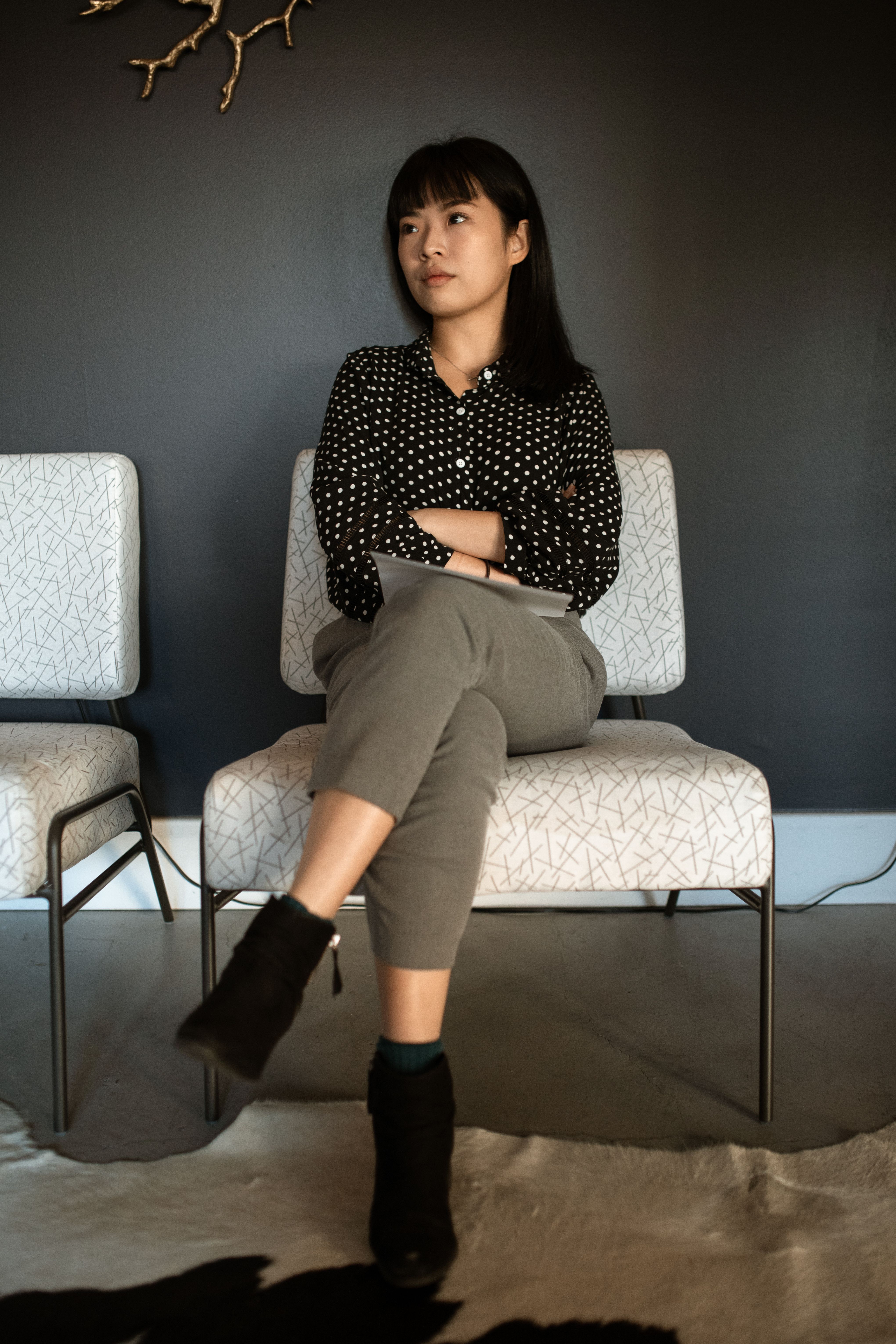 一位年轻女子穿着波尔卡圆点衬衫，在室内交叉双腿坐着