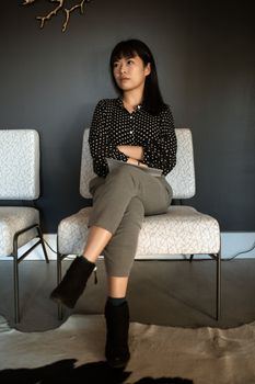 一位年轻女子穿着波尔卡圆点衬衫，在室内交叉双腿坐着
