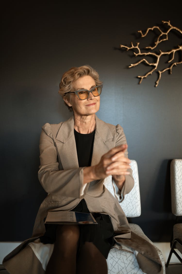 An Elderly Woman In Brown Blazer Sitting On The Chair