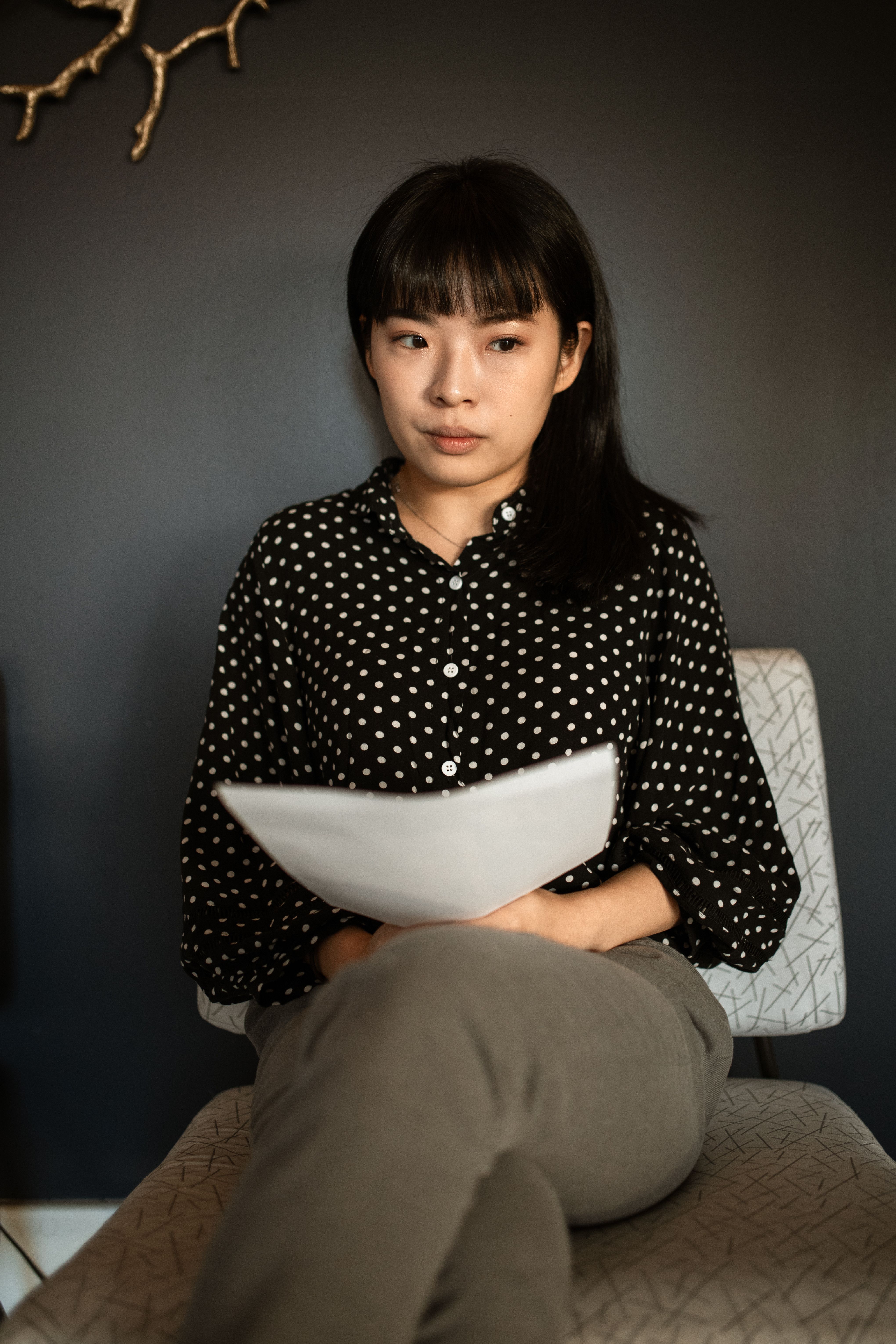 一位亚洲女性坐在室内，手里拿着纸，表情严肃