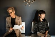 两名女性带着简历，坐在时尚现代的等候区，准备参加面试