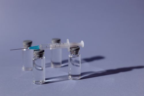 Free A syringe balanced on vaccine vials with a purple backdrop, representing medical treatment. Stock Photo