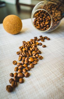 Aesthetic arrangement of coffee beans spilled from a glass jar onto a textured surface.