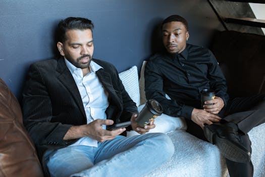 Two businessmen in a modern office lounge discussing work while holding coffee.