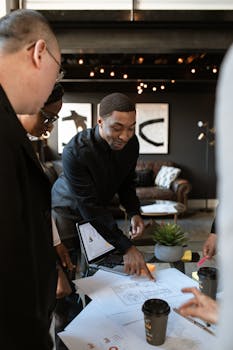 Group of business professionals discussing plans in a stylish, modern office setting with documents and coffee.