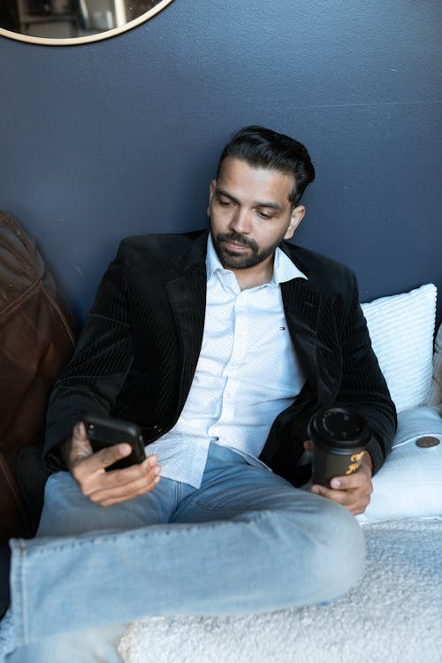 A Man in Black Suit Holding Paper Cup and Cellphone