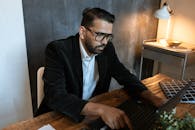 Man in Black Suit Jacket Wearing Black Framed Eyeglasses Working on His Laptop
