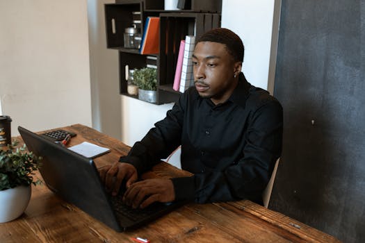 African American man in black shirt typing on laptop at office desk