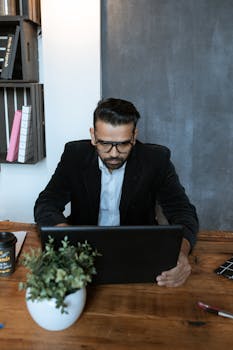 Businessman concentrating on work at an office desk with laptop and coffee.
