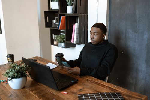 Free Black businessman working at a desk with laptop and phone in modern office setting. Stock Photo
