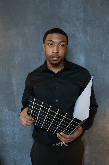 Portrait of a focused Black businessman in a black shirt holding a grid file against a textured wall.