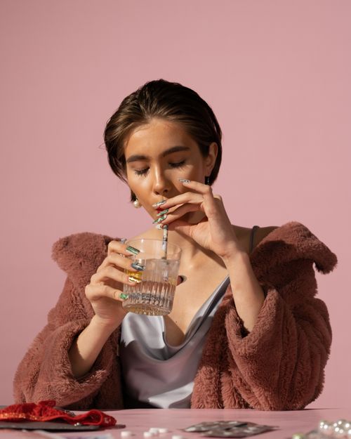 Free A stylish woman in fur coat savors a drink, captured in a minimalist studio setting. Stock Photo
