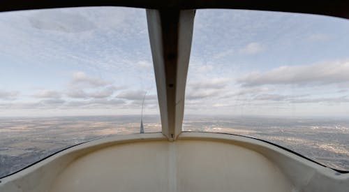 View through windshield of aircraft cockpit soaring over vast plain land under cloudy sky