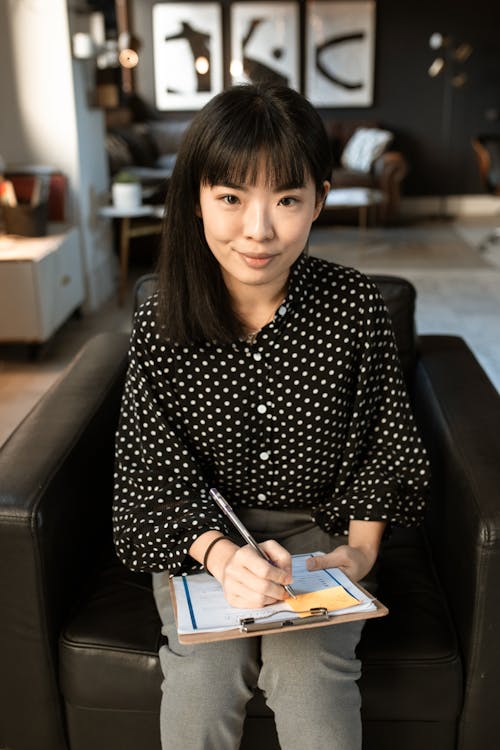 Woman in Black and White Polka Dot Long Sleeve Shirt Sitting on Black Leather Couch