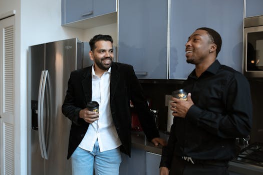 Two diverse professionals enjoying coffee and conversation in an office kitchen.