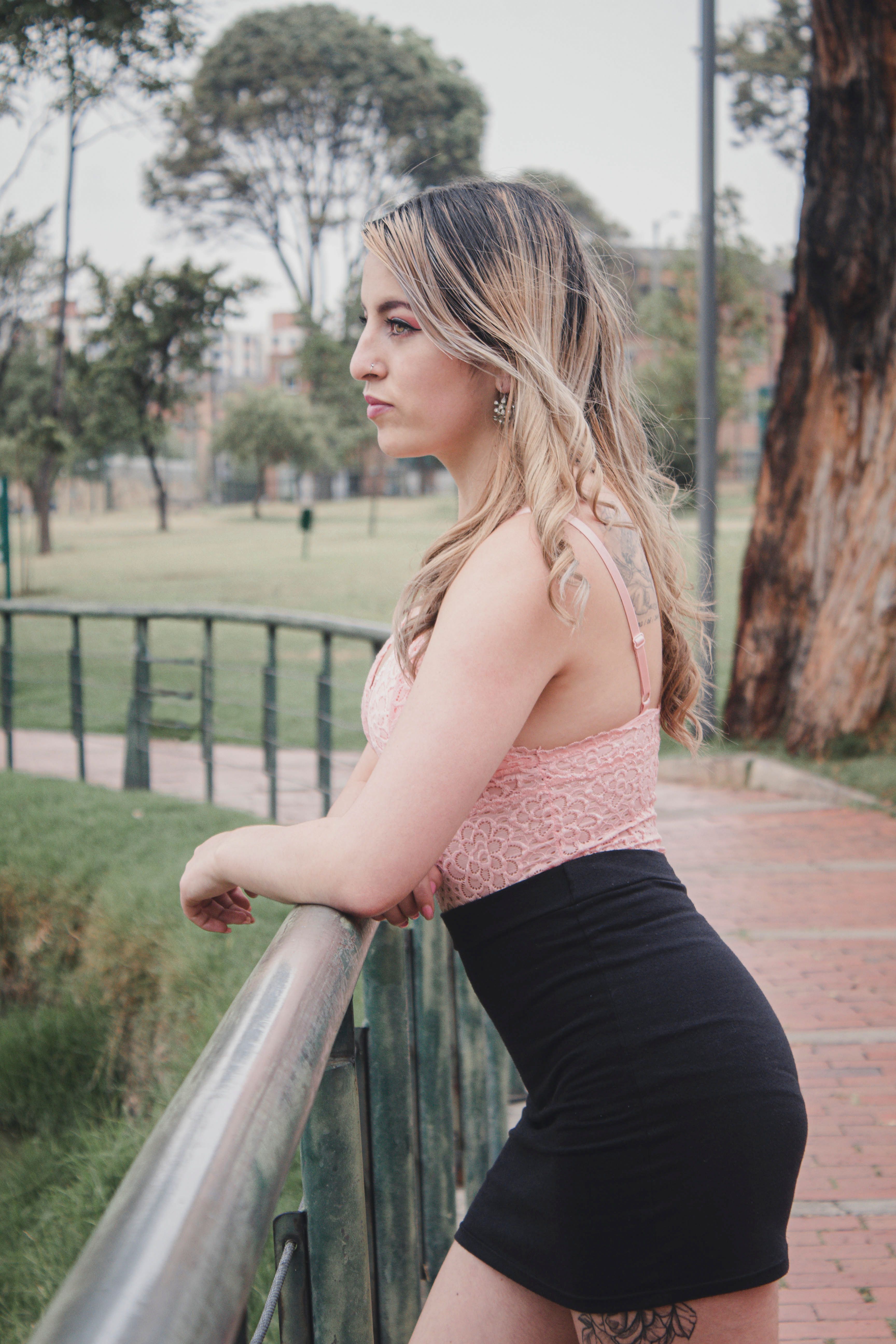 A thoughtful woman stands by a railing in a lush park in Bogota, Colombia, embodying serene contemplation.