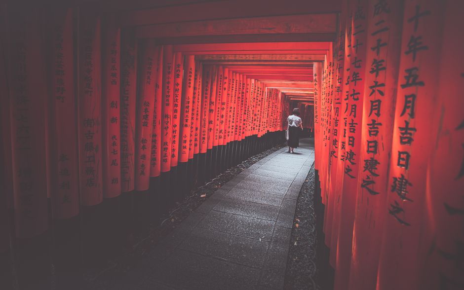 A woman walks through the iconic red torii gates of Fushimi Inari Taisha in Kyoto, Japan.