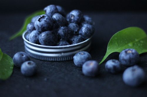 Free A vibrant arrangement of fresh blueberries on a lid surrounded by green leaves. Stock Photo
