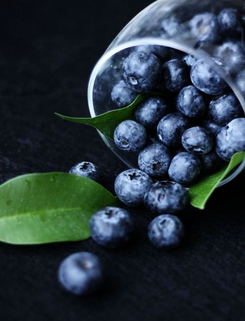 Free Juicy ripe blueberries spilling from a glass with green leaves, perfect for healthy eating themes. Stock Photo