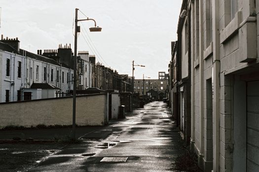 A nostalgic view of a wet, empty city street lined with classic buildings under overcast skies.