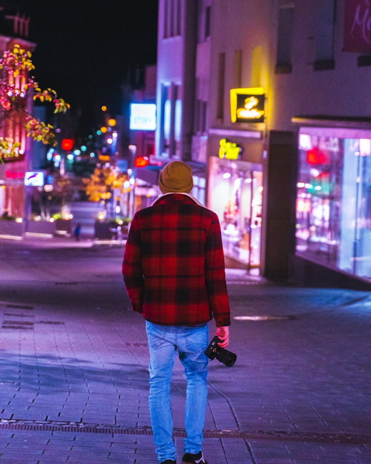 Man Walking Through A City At Night With A Camera