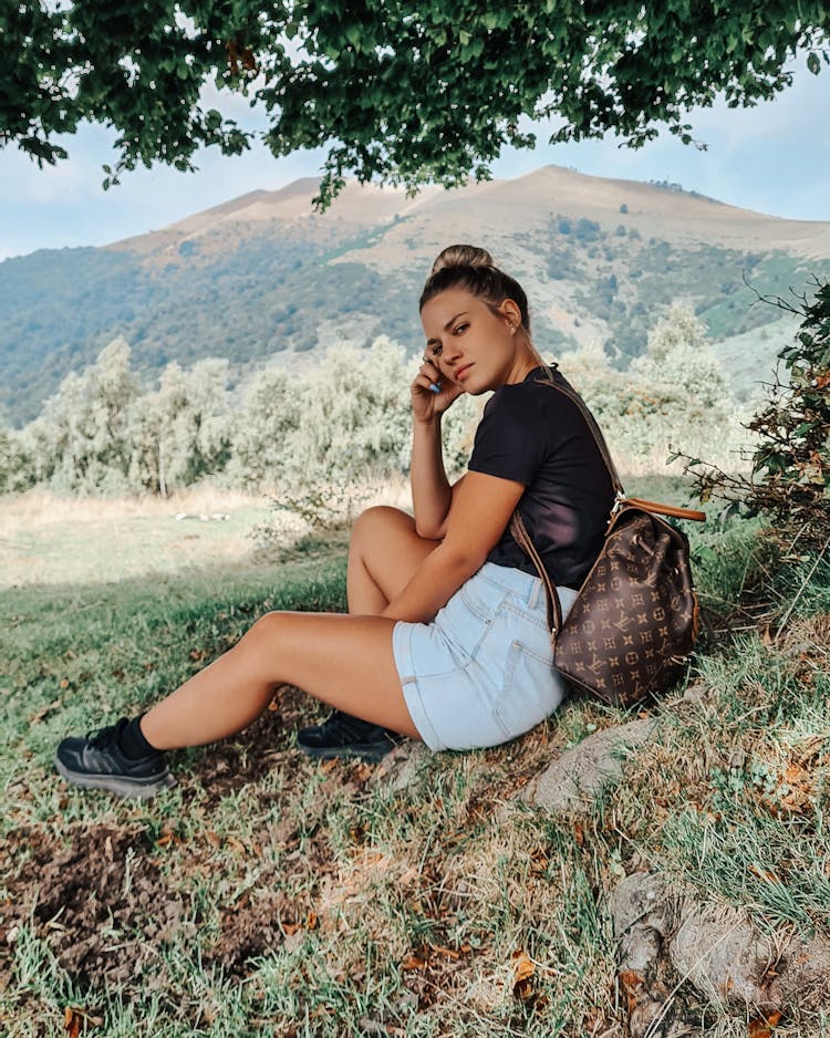 Beautiful Woman With A Backpack Sitting On Green Grass