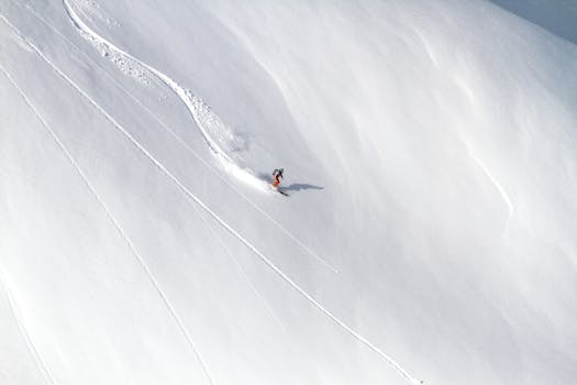 An aerial shot of a skier carving down a snow-covered mountain in winter, leaving a trail behind.