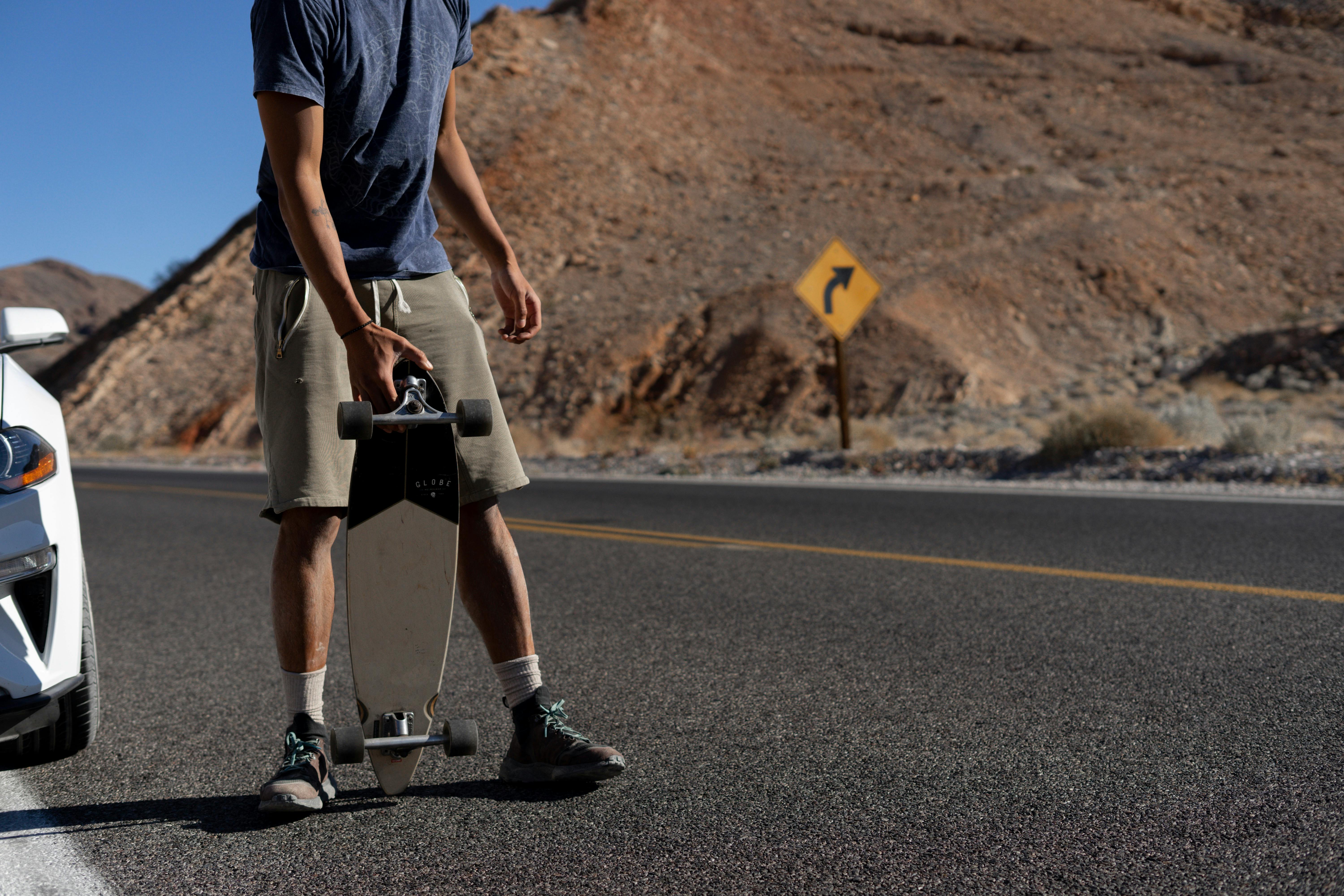 Man with a Longboard Standing on Roadside