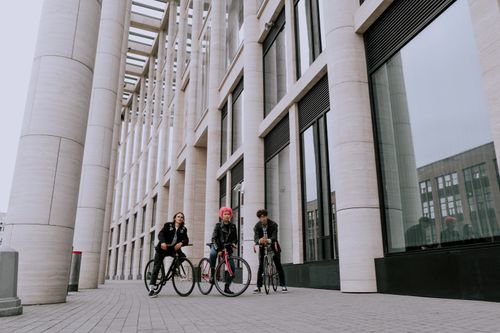 Free Three stylish young adults with bicycles in front of modern architecture embracing urban lifestyle. Stock Photo