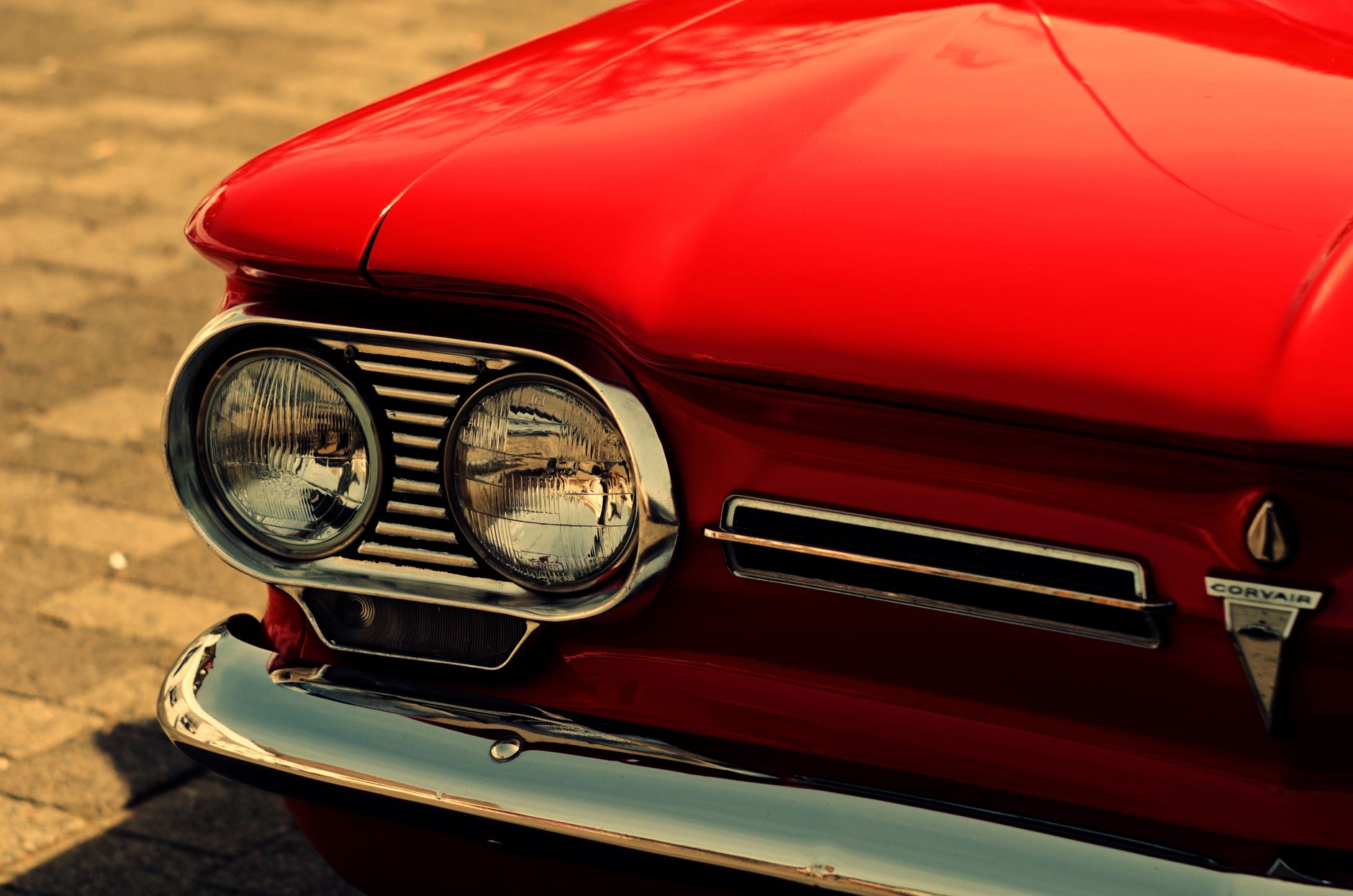 Detailed close-up of a vintage red car showcasing classic headlight and grill design, exuding nostalgia.