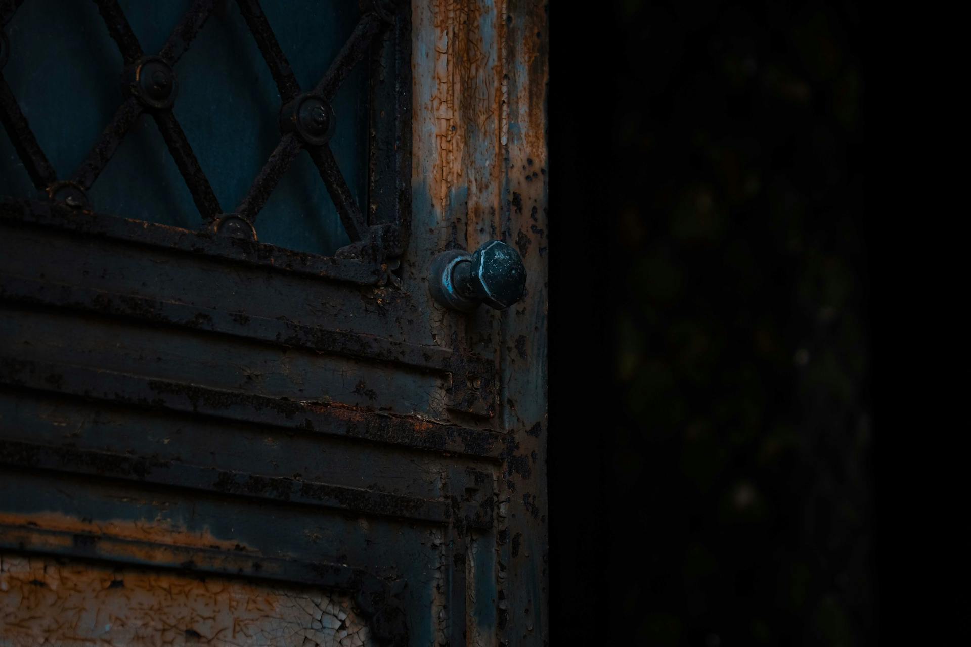 Close-up of an old rusty iron door with a weathered handle, showcasing decay.