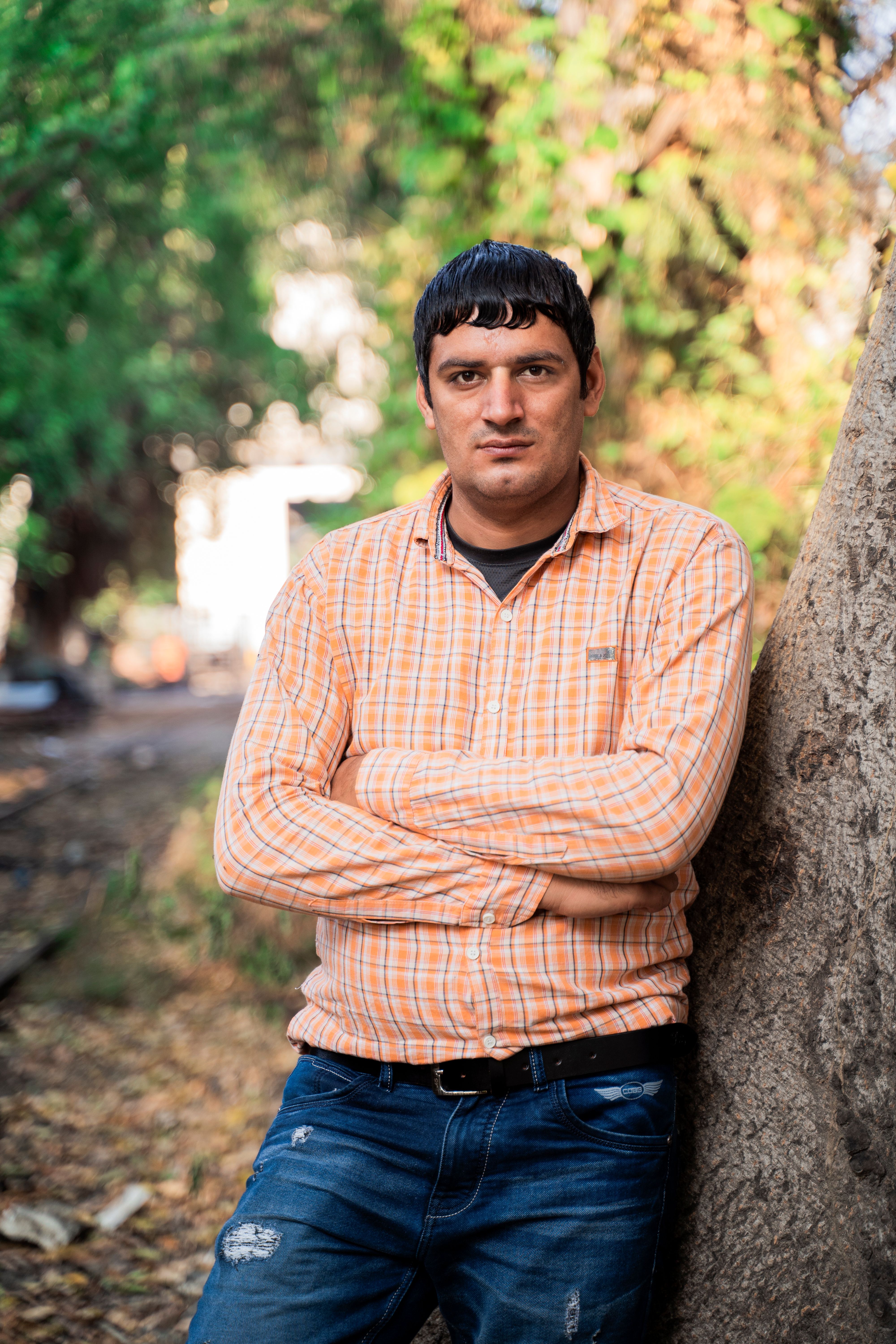 Casual portrait of a man in a plaid shirt leaning against a tree in an outdoor setting.