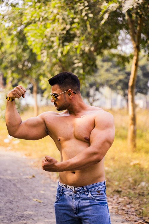 Free Shirtless muscular man flexing his biceps outdoors on a sunny day. Stock Photo