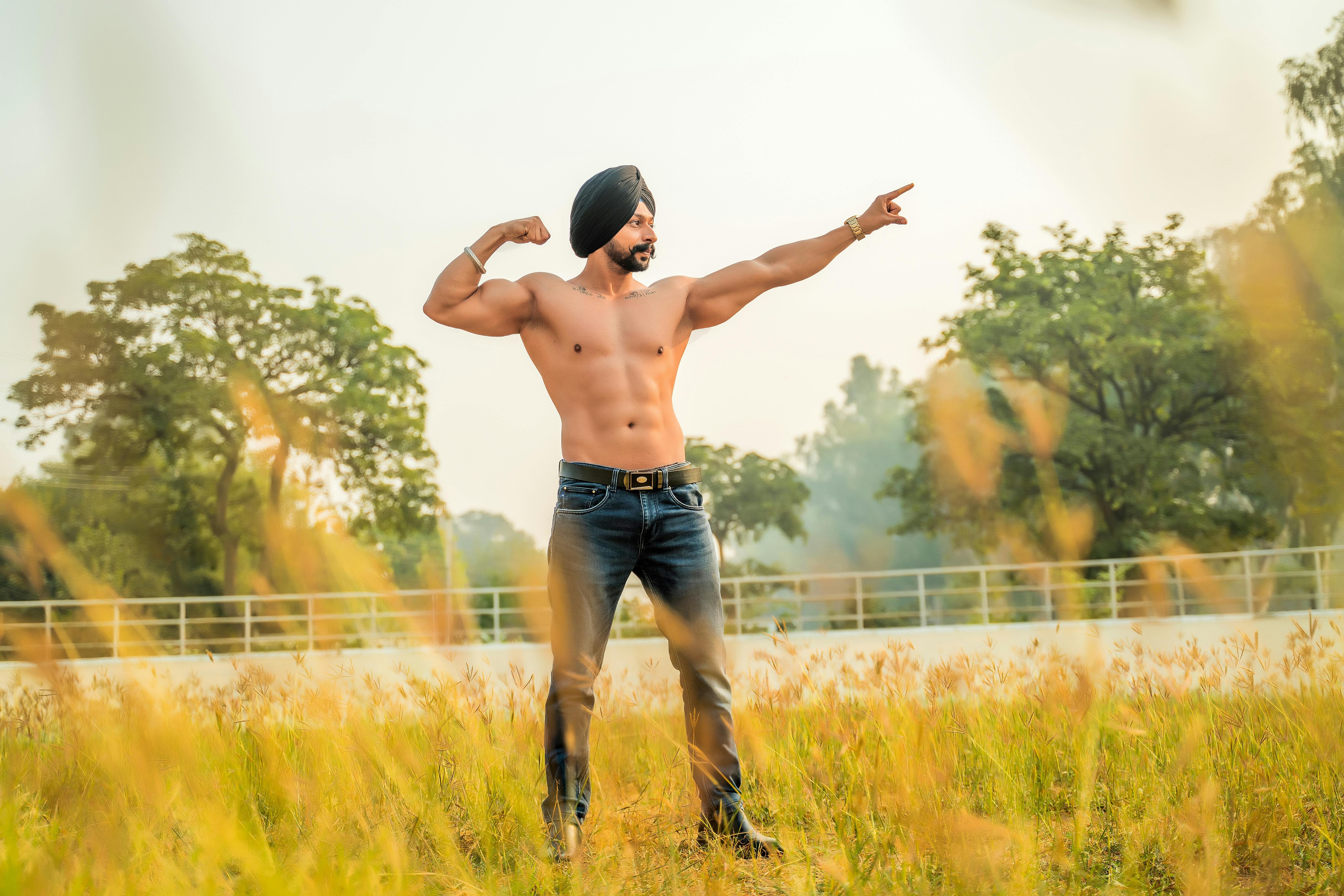 Shirtless muscular man with turban posing outdoors, showcasing strength and confidence in a natural setting.